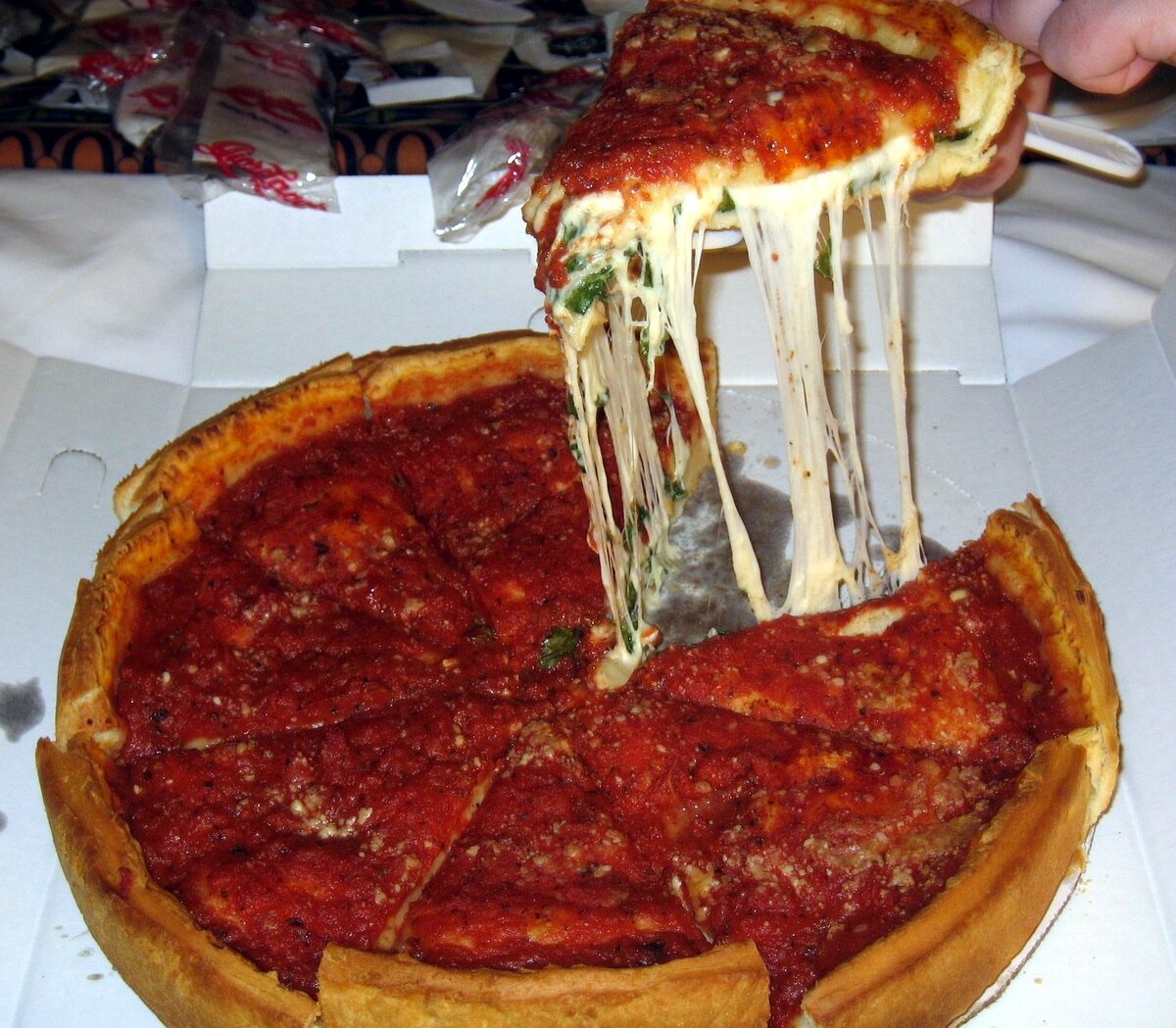 A slice of Giordano's Chicago deep-dish pizza lifted out, trailing melted cheese