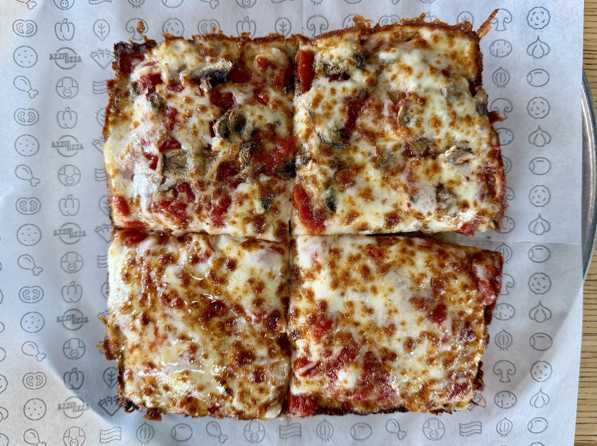 A square Detroit-style pizza cut in four, with browned cheese at the edges