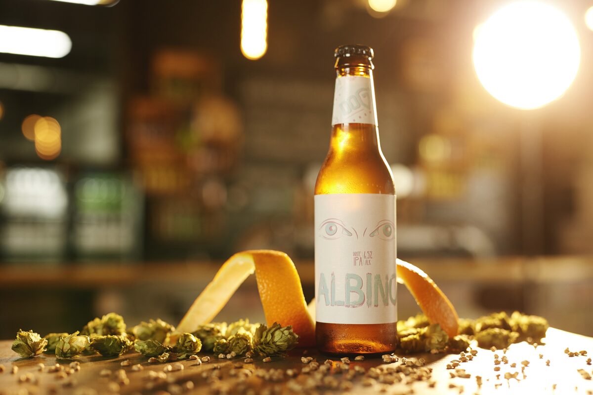 A bottle of Dogma Albino white IPA, a Serbian craft beer, among hop cones and grain