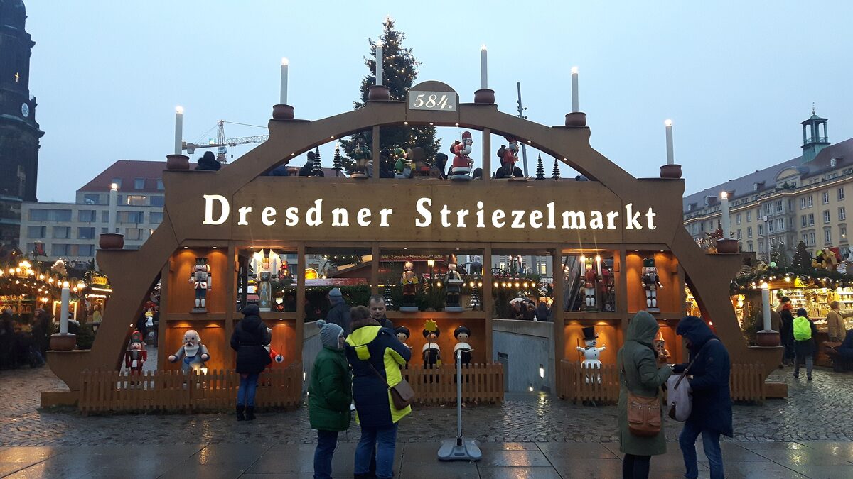 The wooden candle arch of the Dresden Striezelmarkt at dusk, with the Christmas tree behind