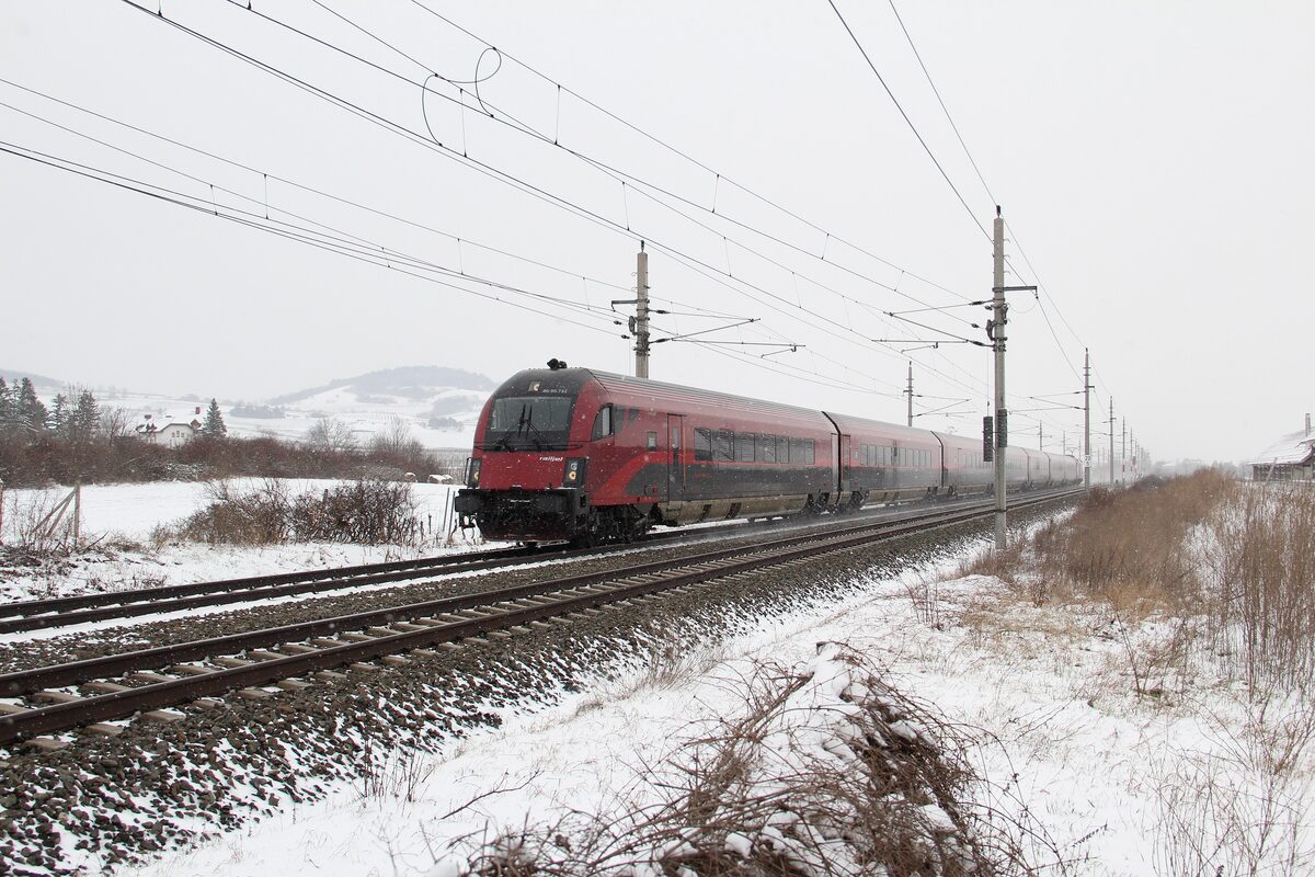An Austrian Railjet train running through a snowy winter landscape