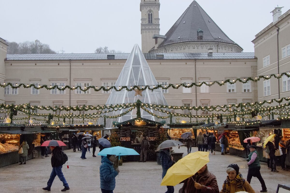 Visitors with umbrellas among the stalls of the Salzburg Christkindlmarkt on Domplatz