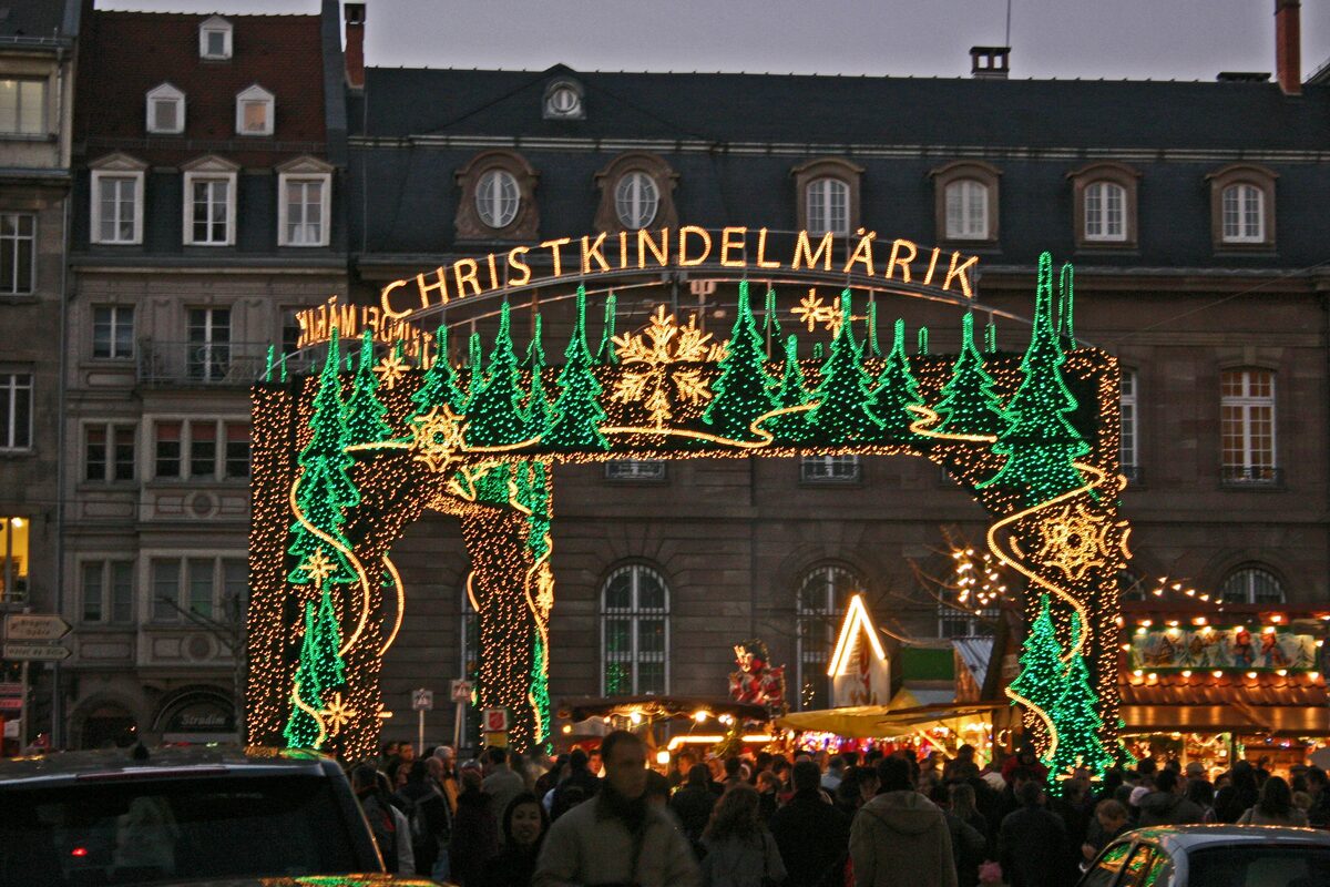 The lit Christkindelsmärik gate over a crowd at the Strasbourg Christmas market