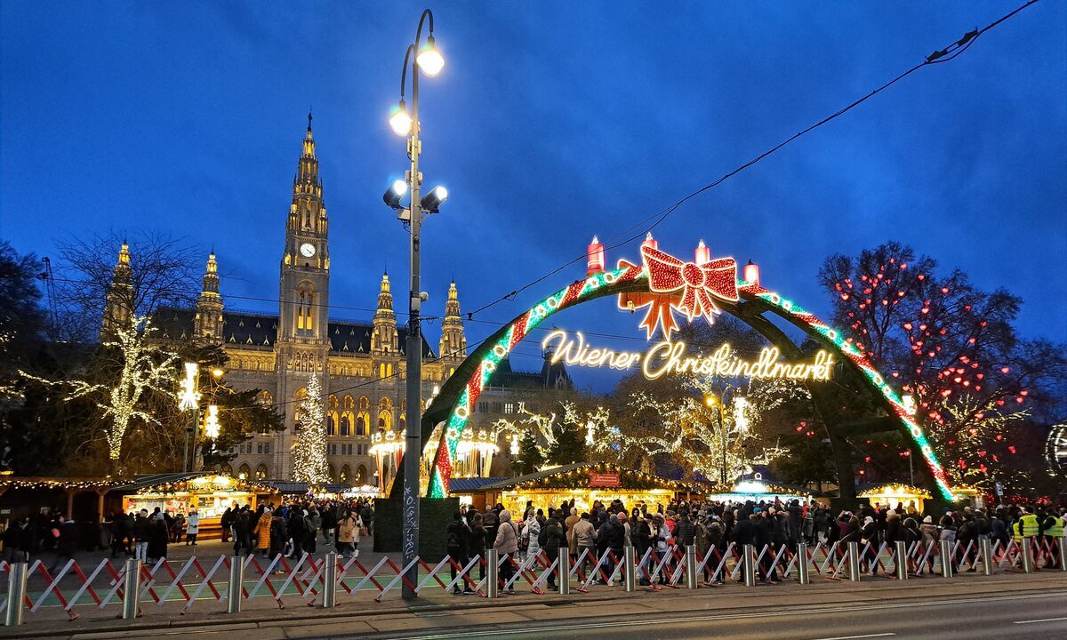 The lit Wiener Christkindlmarkt arch with Vienna City Hall behind it at dusk