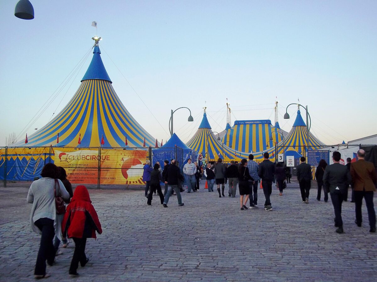 Blue and yellow striped Cirque du Soleil big top at the Old Port of Montreal, with visitors walking toward the entrance