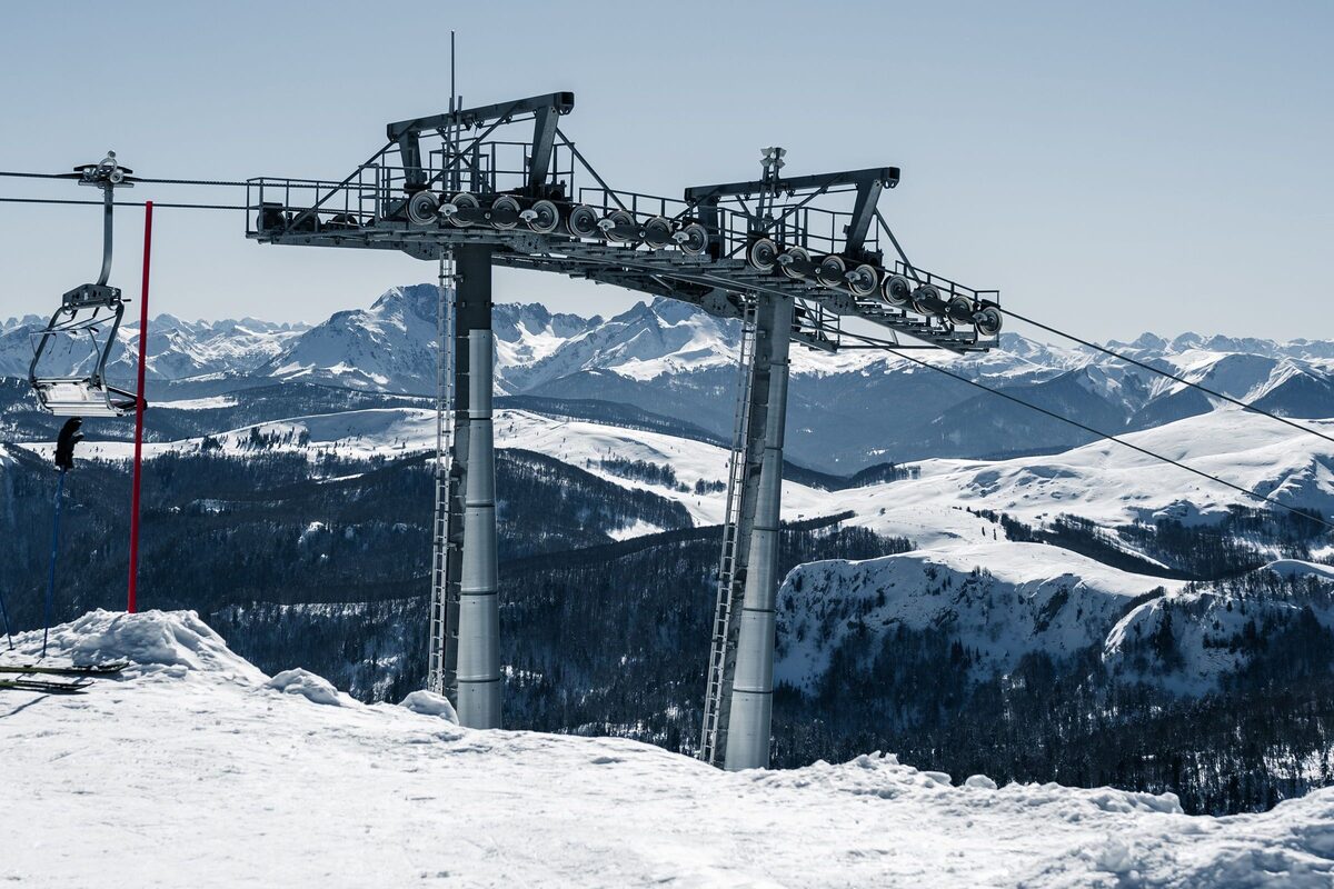A chairlift tower and a chair at a snowy summit above Kolasin in Montenegro, with mountain ranges behind