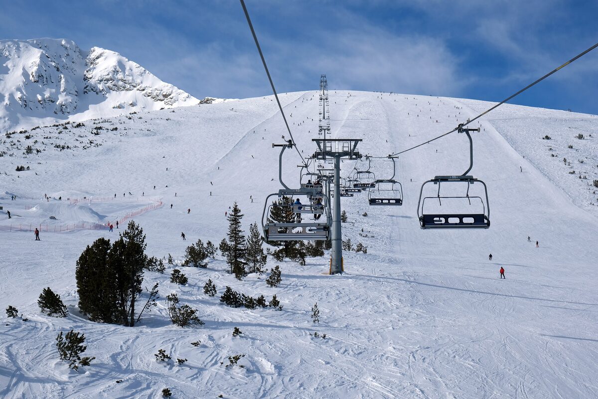 A chairlift running up a snowy slope in the Bansko ski area, with a rocky peak behind