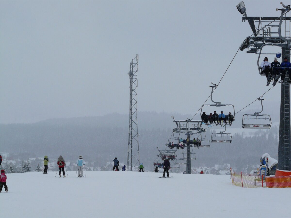 A chairlift and skiers on a low, gentle snowy slope under a grey sky at Kotelnica in the Polish Tatras