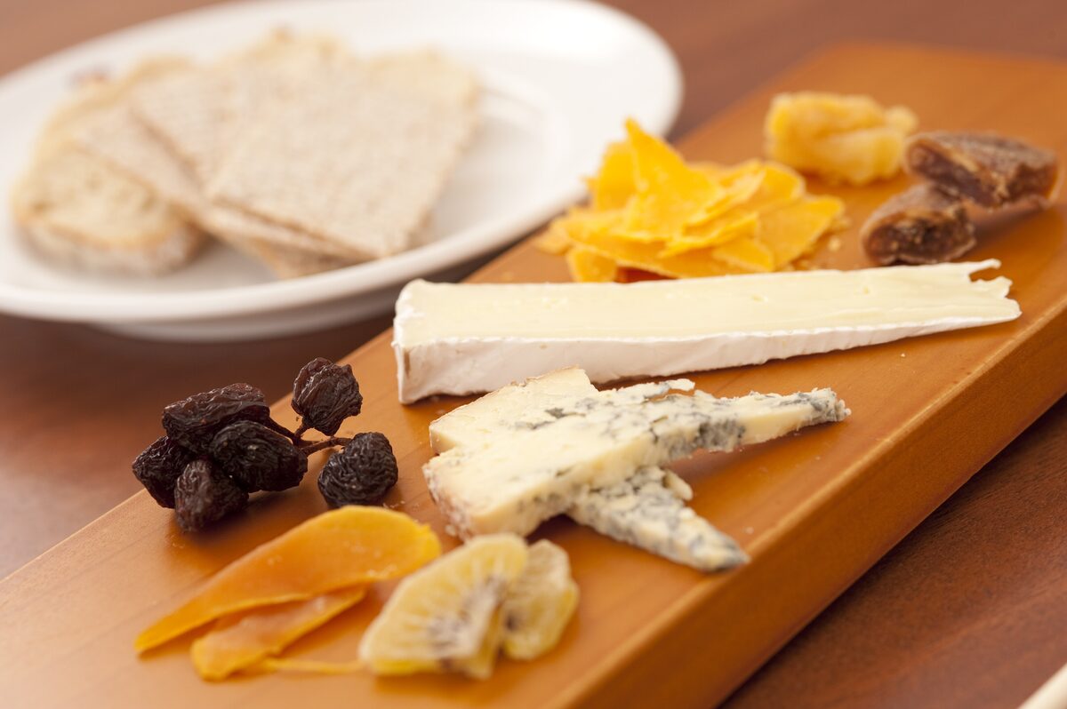 A wooden board with soft, blue and hard cheeses, dried fruit and crackers
