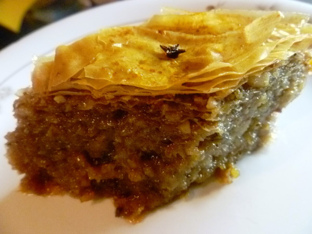 A slice of Greek baklava with a clove on top, layered filo over a ground-nut filling
