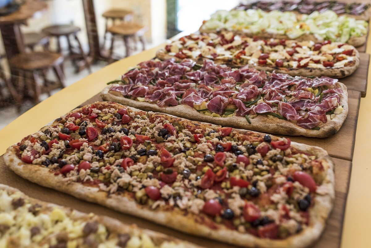 Long rectangular pizzas with different toppings on wooden boards at a pizza al taglio counter