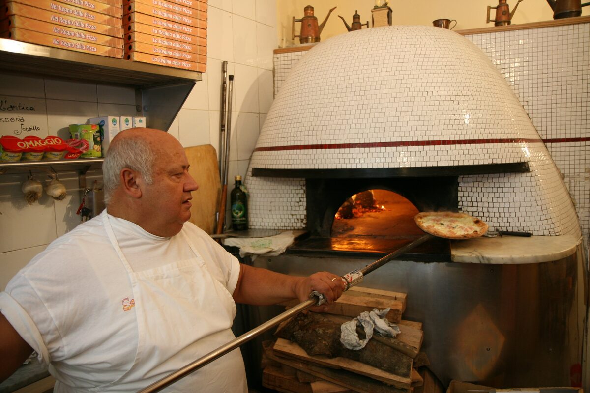 A pizza maker sliding a pizza into a tiled dome wood-fired oven at Sorbillo in Naples