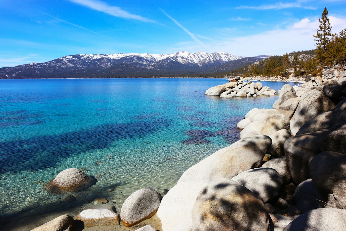 Clear blue water of Lake Tahoe surrounded by pine forest and the Sierra Nevada mountains