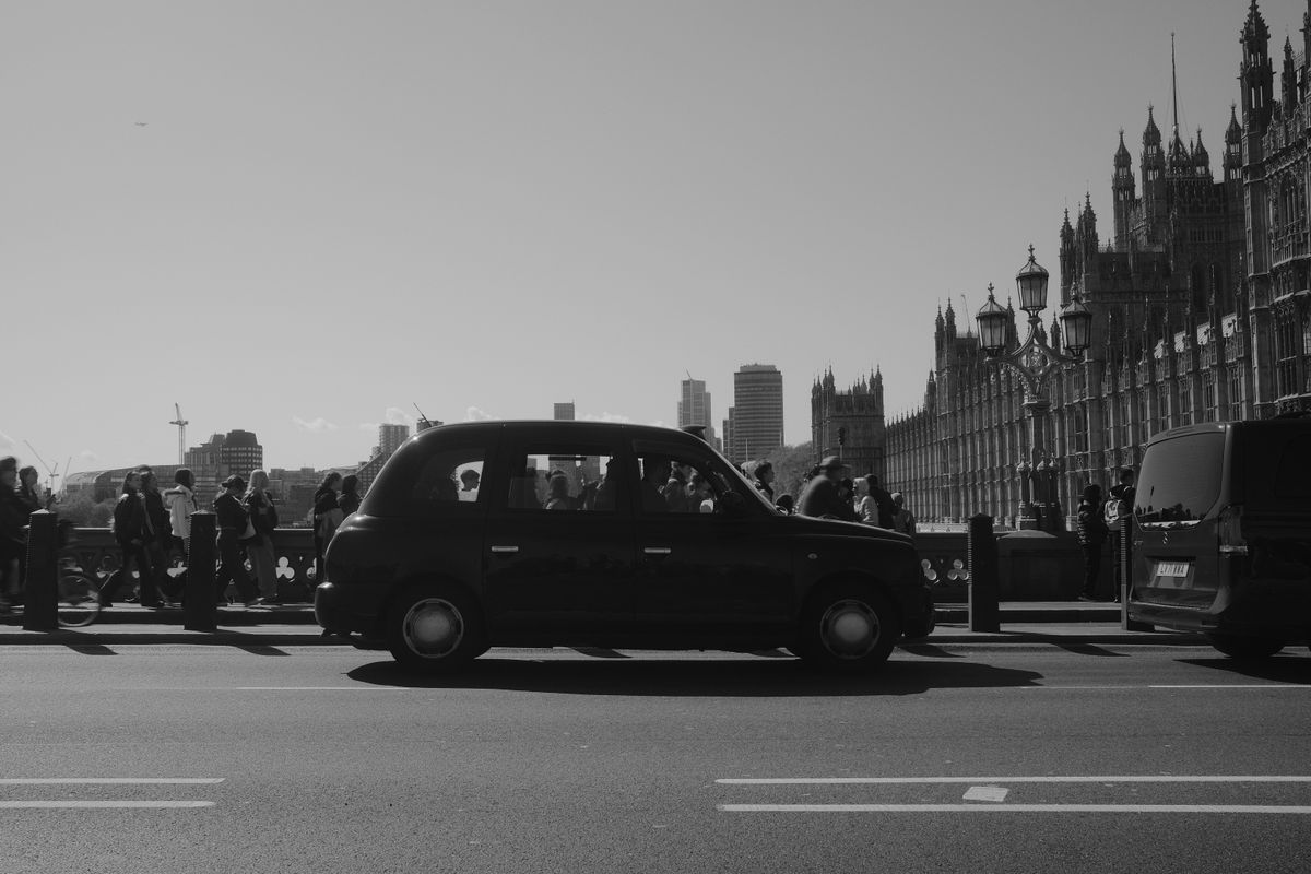 Black and white photo of a traditional London black cab on Westminster Bridge with the Houses of Parliament behind it