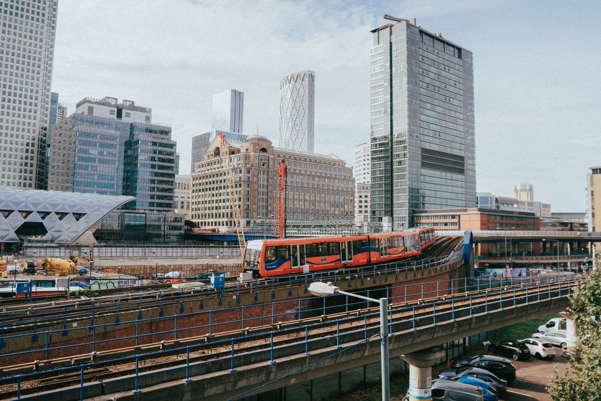 A red and blue Docklands Light Railway train on an elevated track in front of the office towers of Canary Wharf