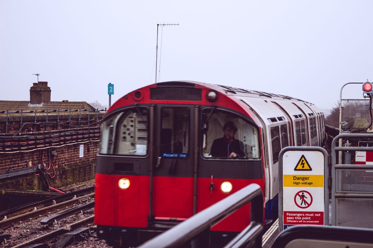 A red, white and blue Piccadilly line train pulling into an above-ground platform on a grey London day