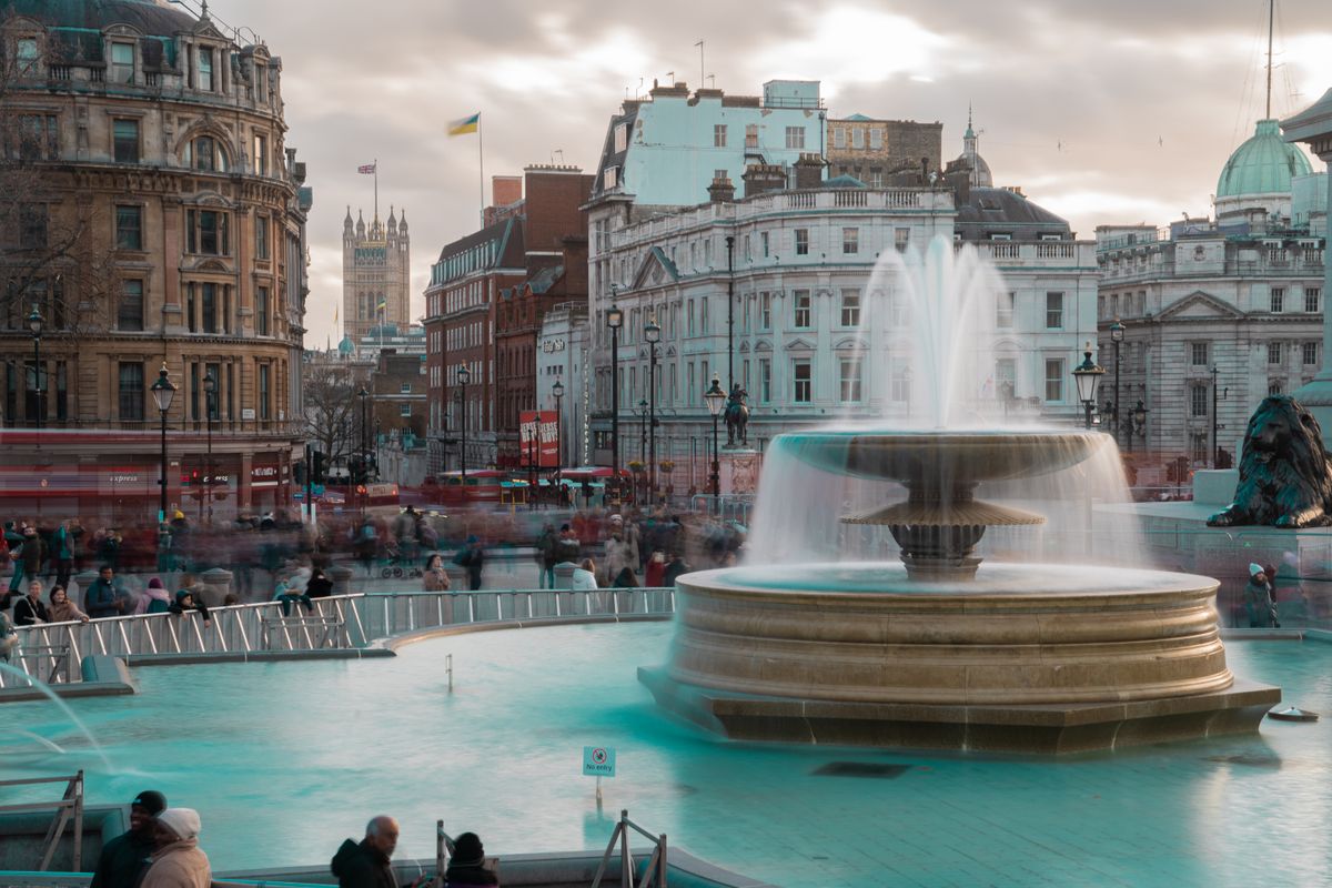 The fountain in Trafalgar Square with crowds around it and the grand buildings of Charing Cross and Whitehall behind