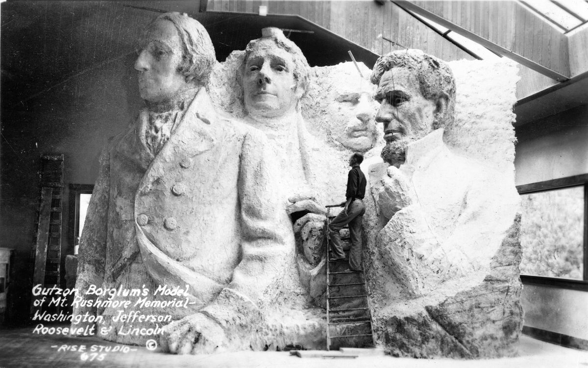 Gutzon Borglum's plaster model of Mount Rushmore, with a figure working beside it
