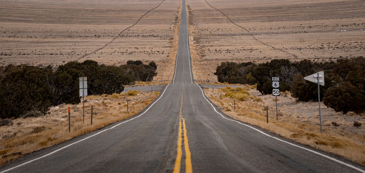 Empty two-lane US 50 across a sagebrush basin in eastern Nevada, with a US 6 and US 50 route sign
