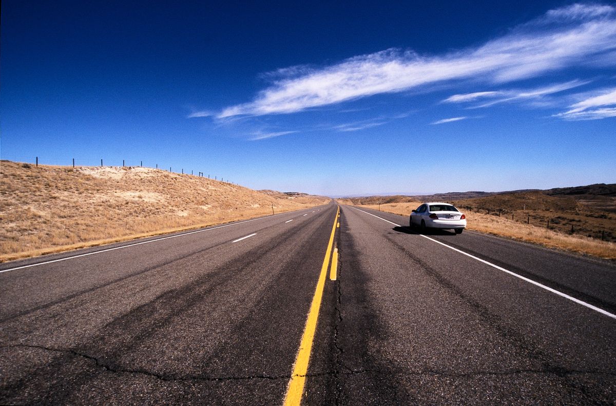 White sedan on an empty highway in rural Wyoming under a deep blue sky