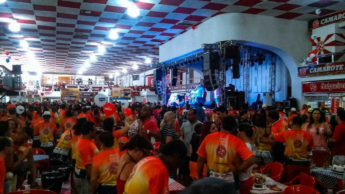 Packed samba school quadra in Rio with a crowd in red and orange shirts in front of the stage