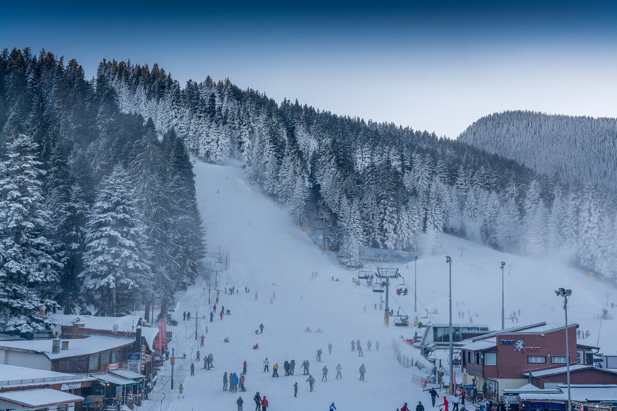 A snowy piste lined with frosted spruce trees and dotted with skiers above the Borovets base area