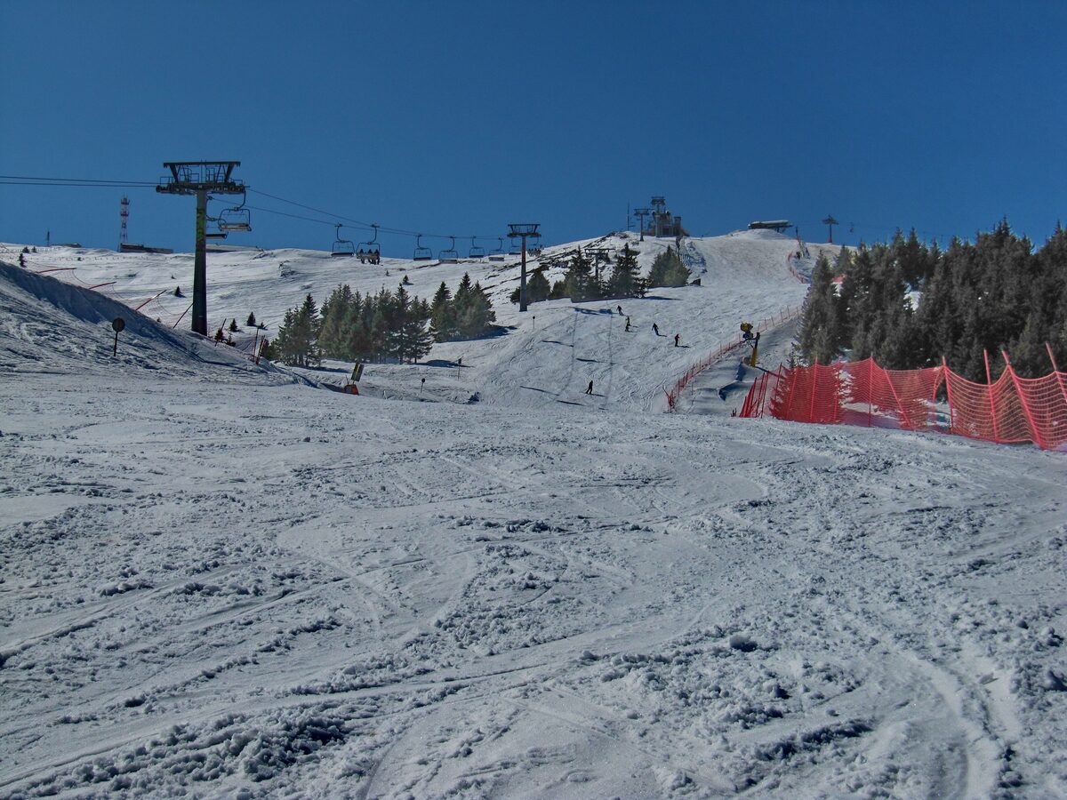 A groomed run and chairlift pylons on a snowy Kopaonik slope under a blue sky