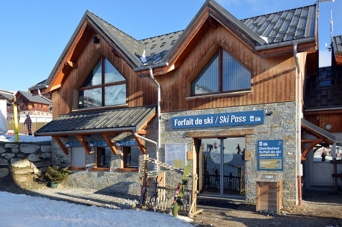 A wood and stone ski pass office with a Forfait de ski / Ski Pass sign and a ticket machine at La Toussuire