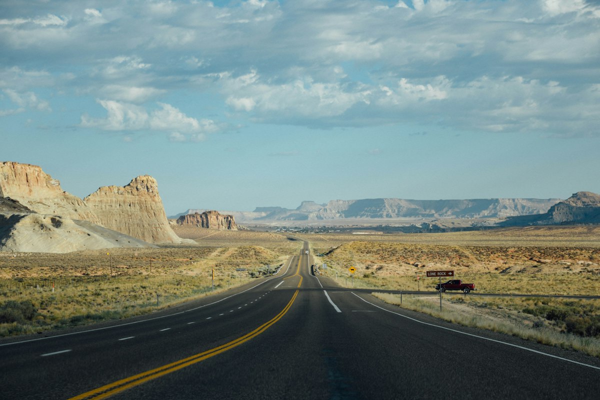Empty highway running through the Utah desert at sunrise under a big cloudy sky