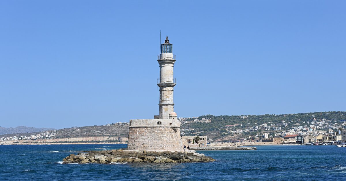 The old lighthouse at the entrance to Chania's old harbor, with the town and hills behind