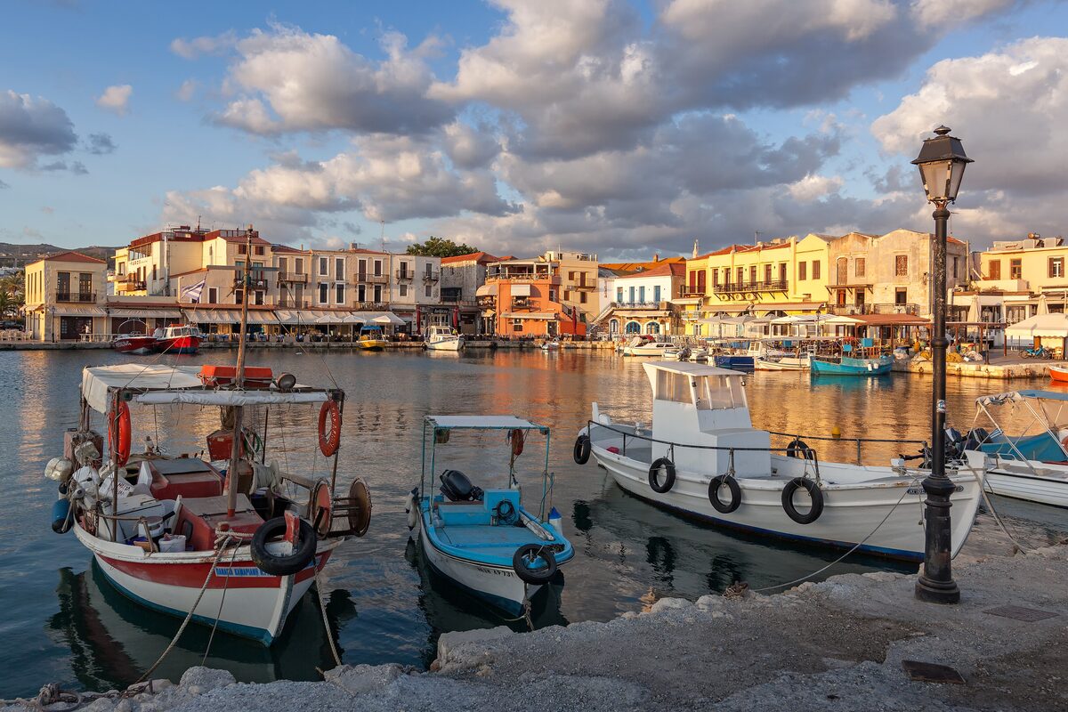 Fishing boats in Rethymno's small Venetian harbor, with tavernas along the quay under a cloudy morning sky