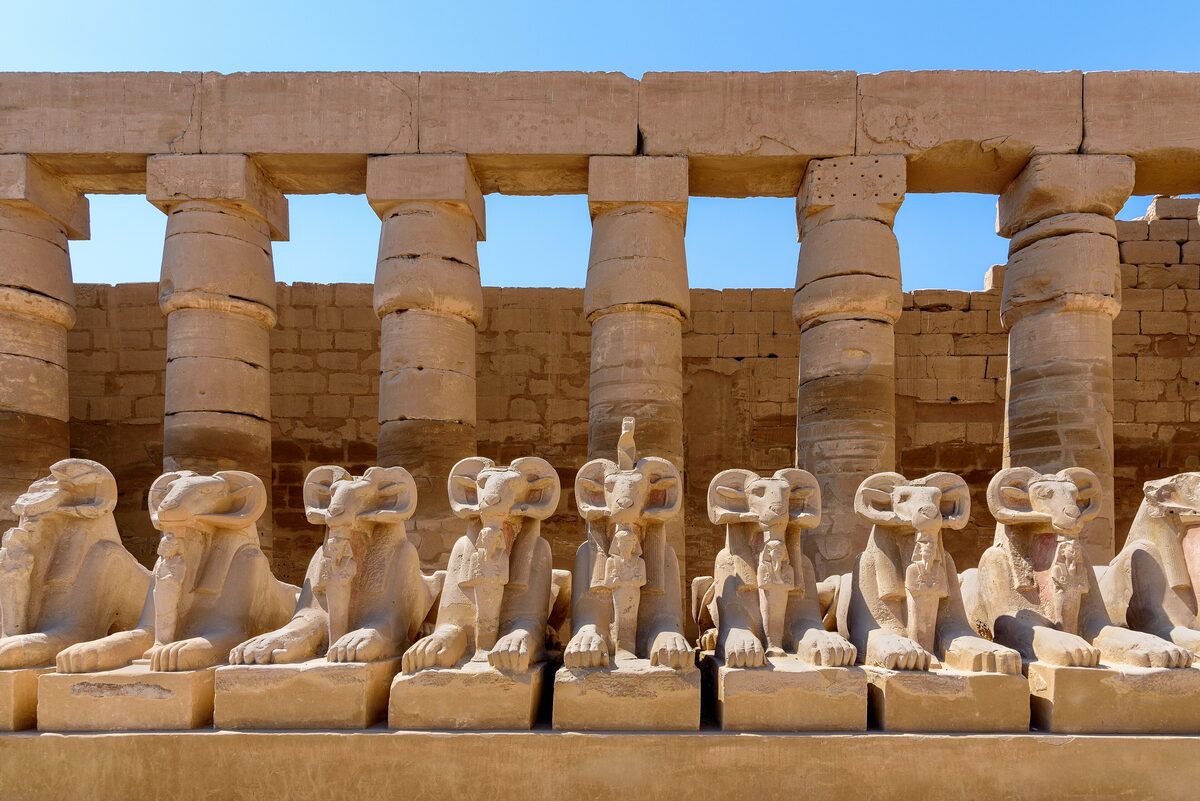 A row of ram-headed sphinxes in front of a colonnade at the Karnak temple complex in Luxor