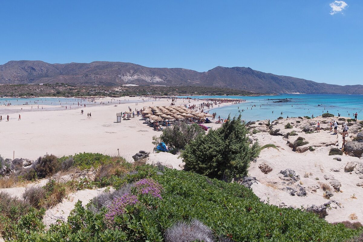 The pale sand and shallow turquoise water of Elafonisi beach on the southwest coast of Crete, with mountains behind