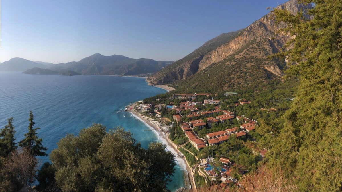 Resort hotels along a curving beach at Oludeniz on the Turkish Mediterranean, with mountains behind