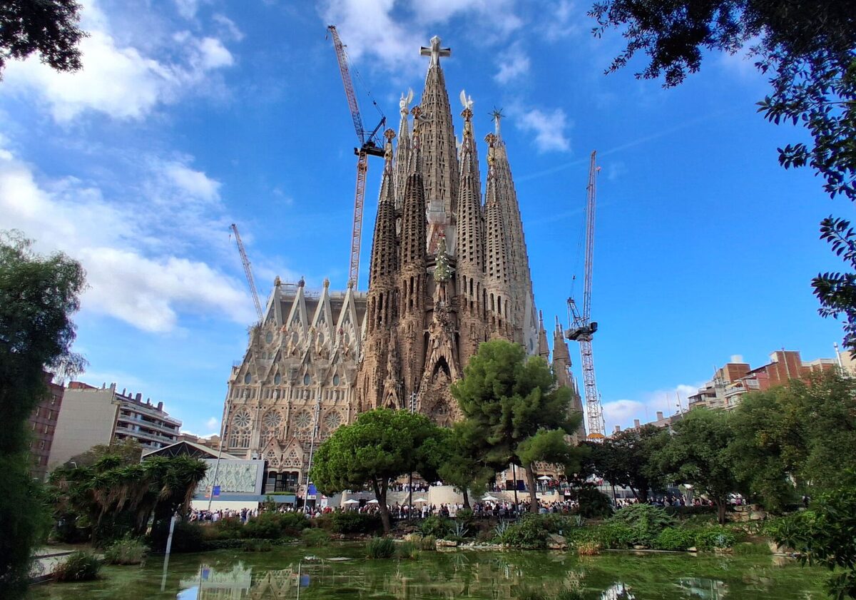 The towers of the Sagrada Família in Barcelona, seen across a pond and trees