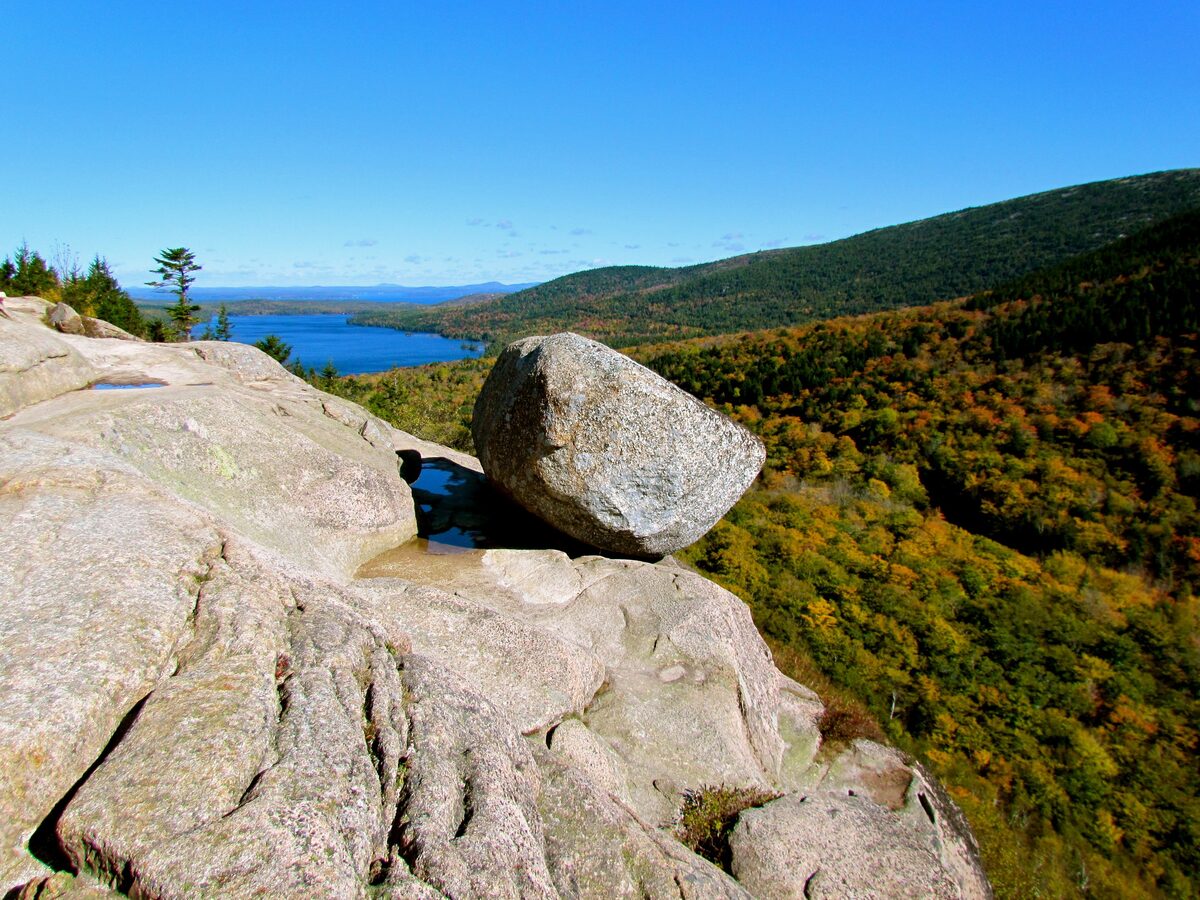 Bubble Rock balanced on a granite ledge above autumn forest and lake