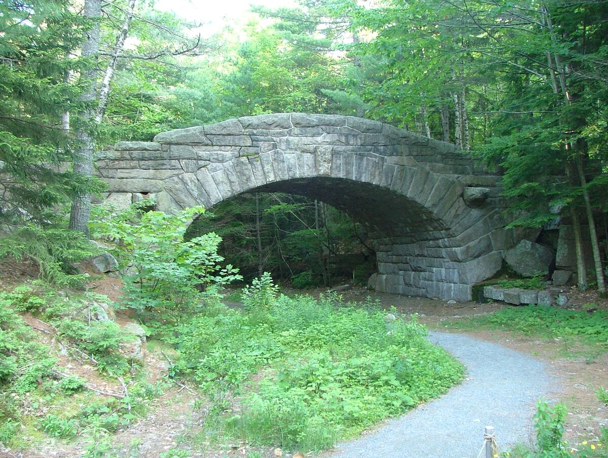 A granite arch bridge over a gravel carriage road in forest