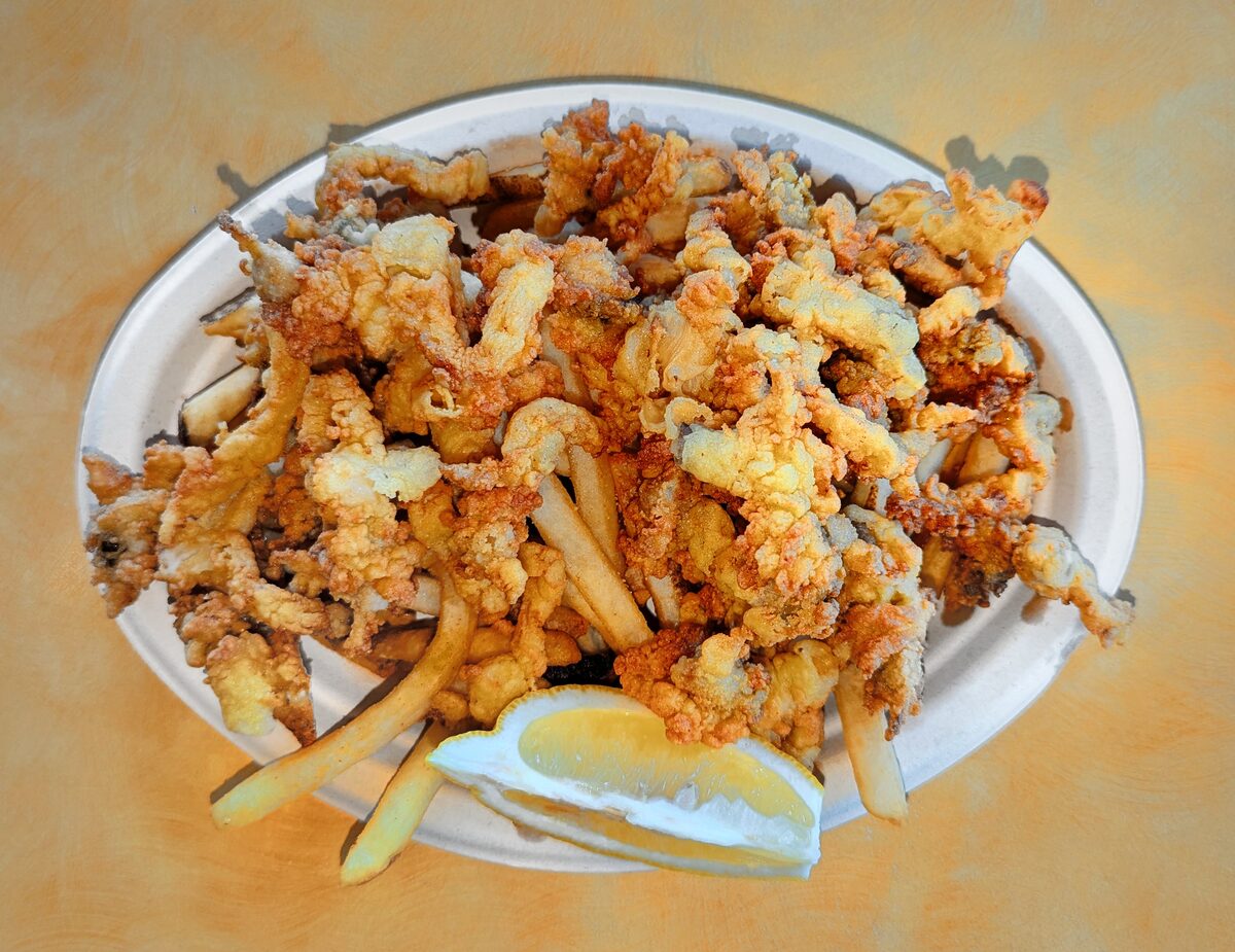 A plate of golden fried clams with French fries and lemon