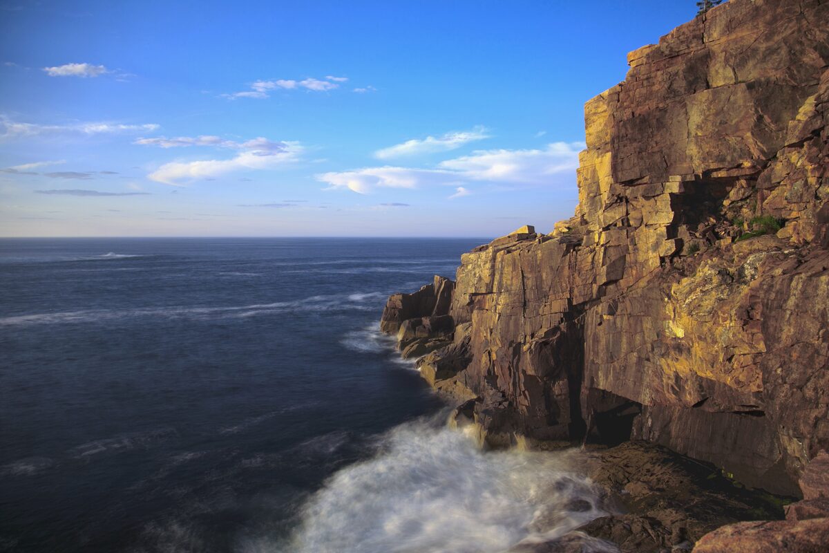 Sunlit granite face of Otter Cliff above dark Atlantic waves