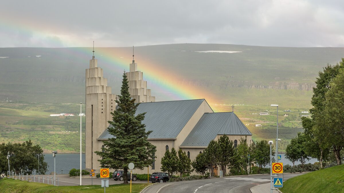 Akureyrarkirkja under a rainbow, its two stepped concrete towers rising above the roofs and the fjord behind