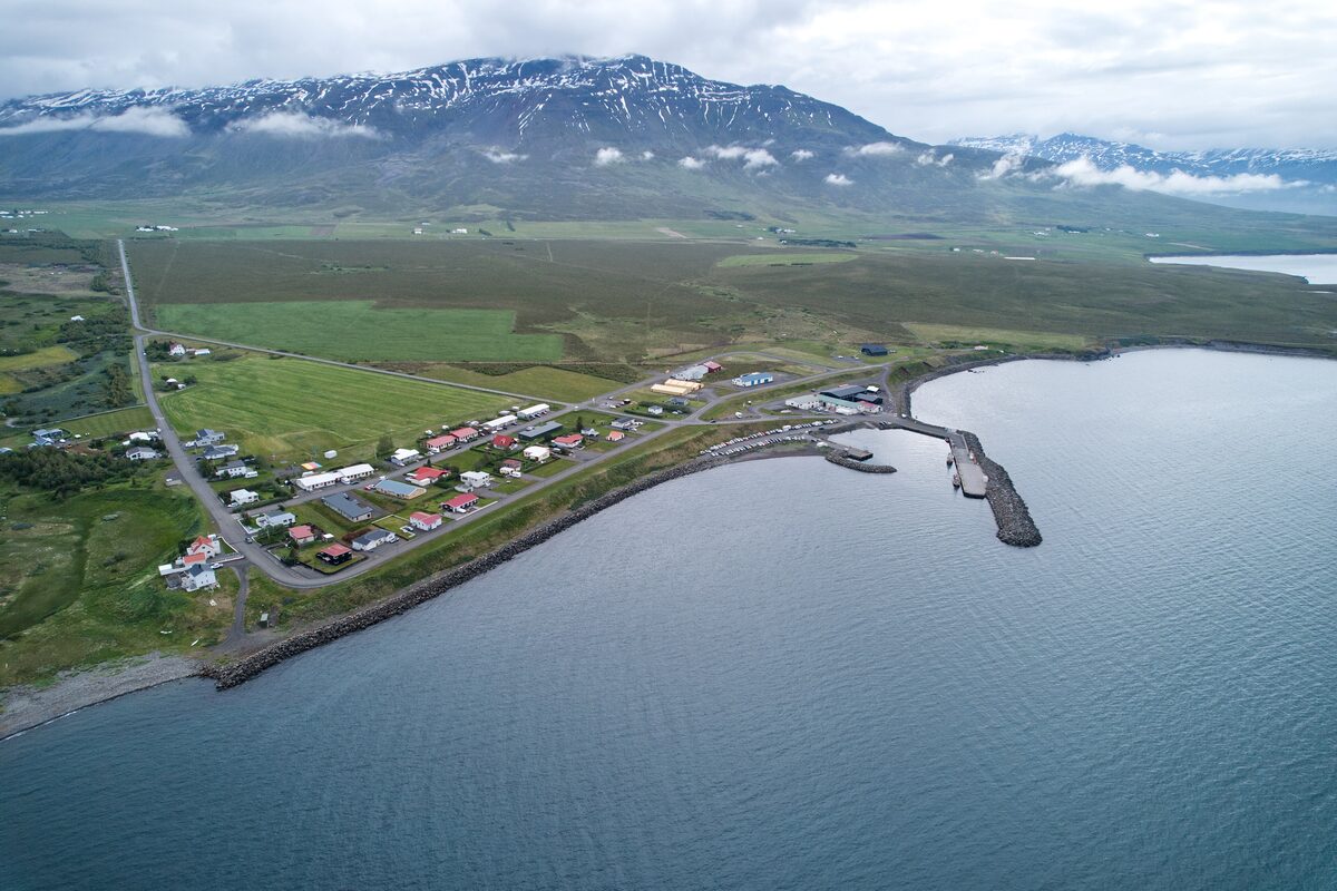 Aerial view of Árskógssandur, a small harbor village on the shore of Eyjafjörður with snowy mountains behind