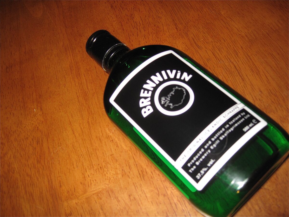 A green bottle of Brennivín with its black and white label on a wooden table