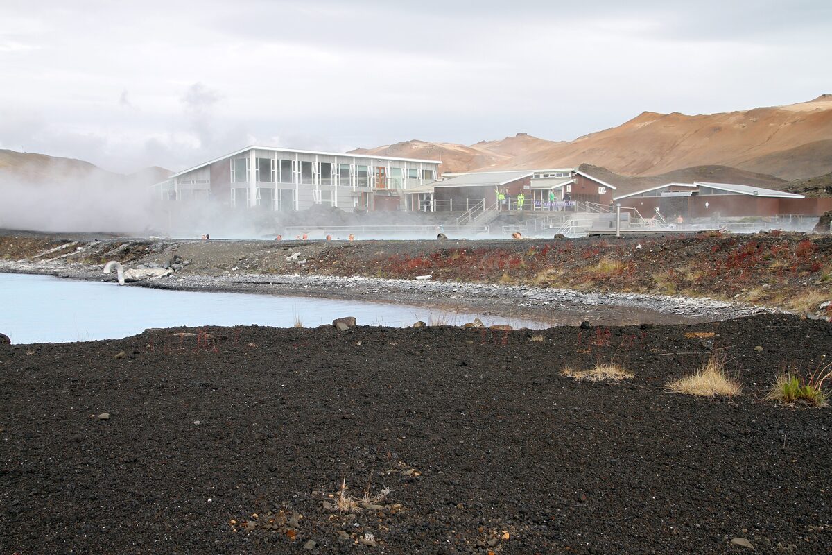 The Earth Lagoon bath buildings on a black lava shore, with steam rising from the geothermal field