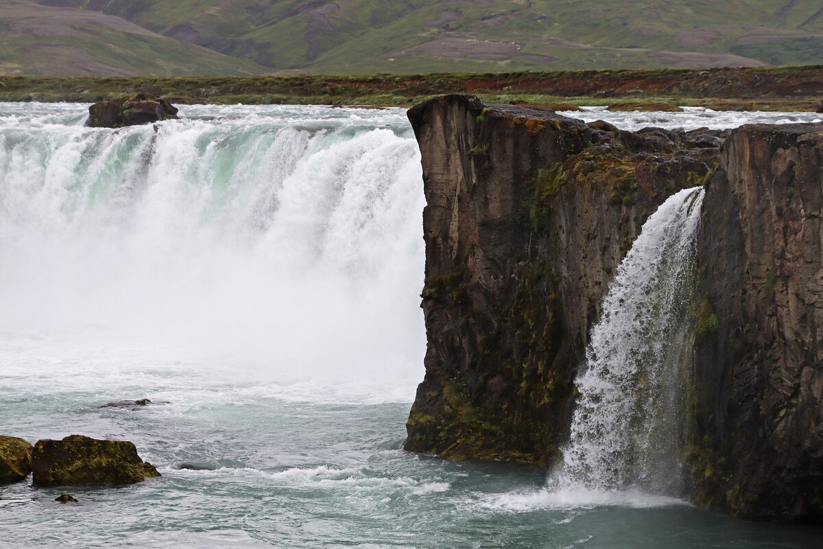 Goðafoss in full flow, white water pouring over the horseshoe edge and a second thin fall dropping beside a dark basalt pillar