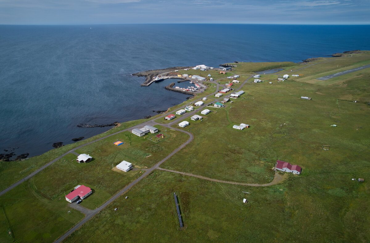 Aerial view of Grímsey village, a cluster of small houses on green grass beside the sea