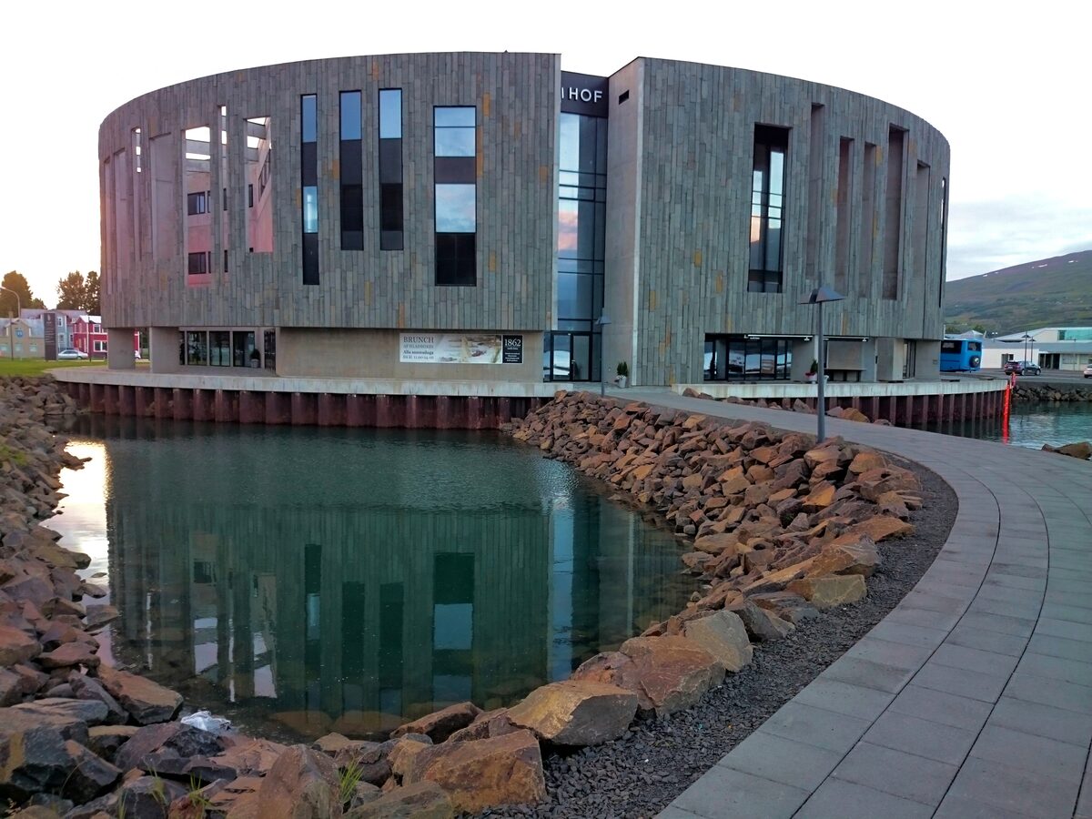 The Hof cultural centre by the harbor, its curved grey stone cladding reflected in a pond edged with rust-colored boulders