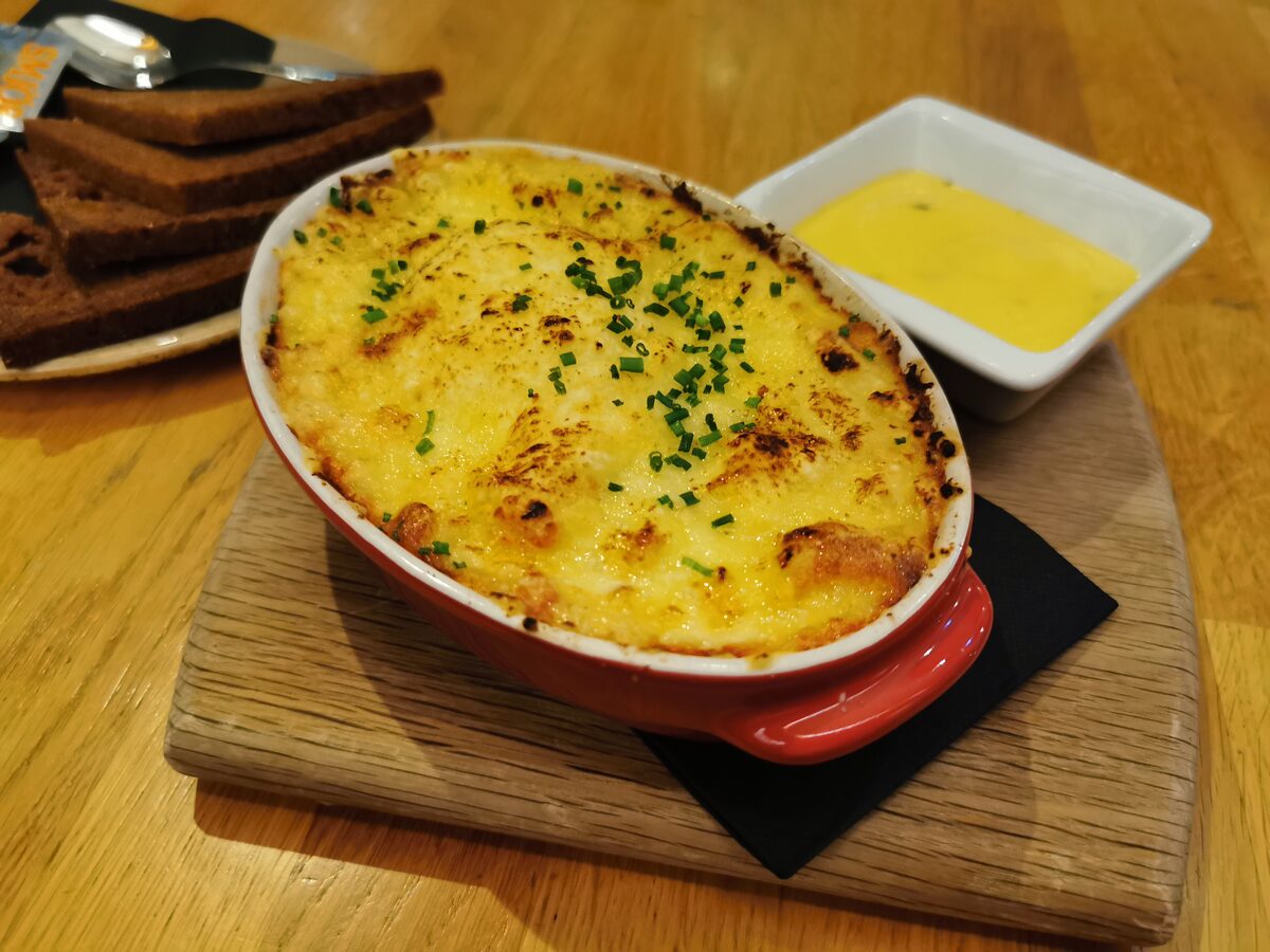 Plokkfiskur baked in a red dish with a golden crust and chives, with dark rye bread and a yellow sauce on the side
