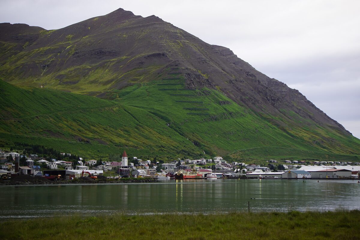 Siglufjörður at the foot of a steep green mountain slope, the town and harbor beside the fjord