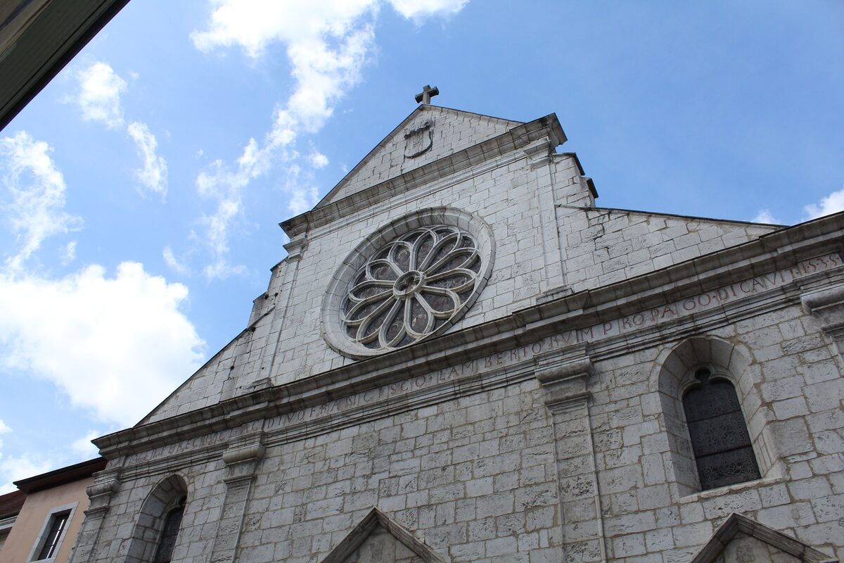 The gable and rose window of the Cathédrale Saint-Pierre in Annecy, set in pale stone against a blue sky with clouds