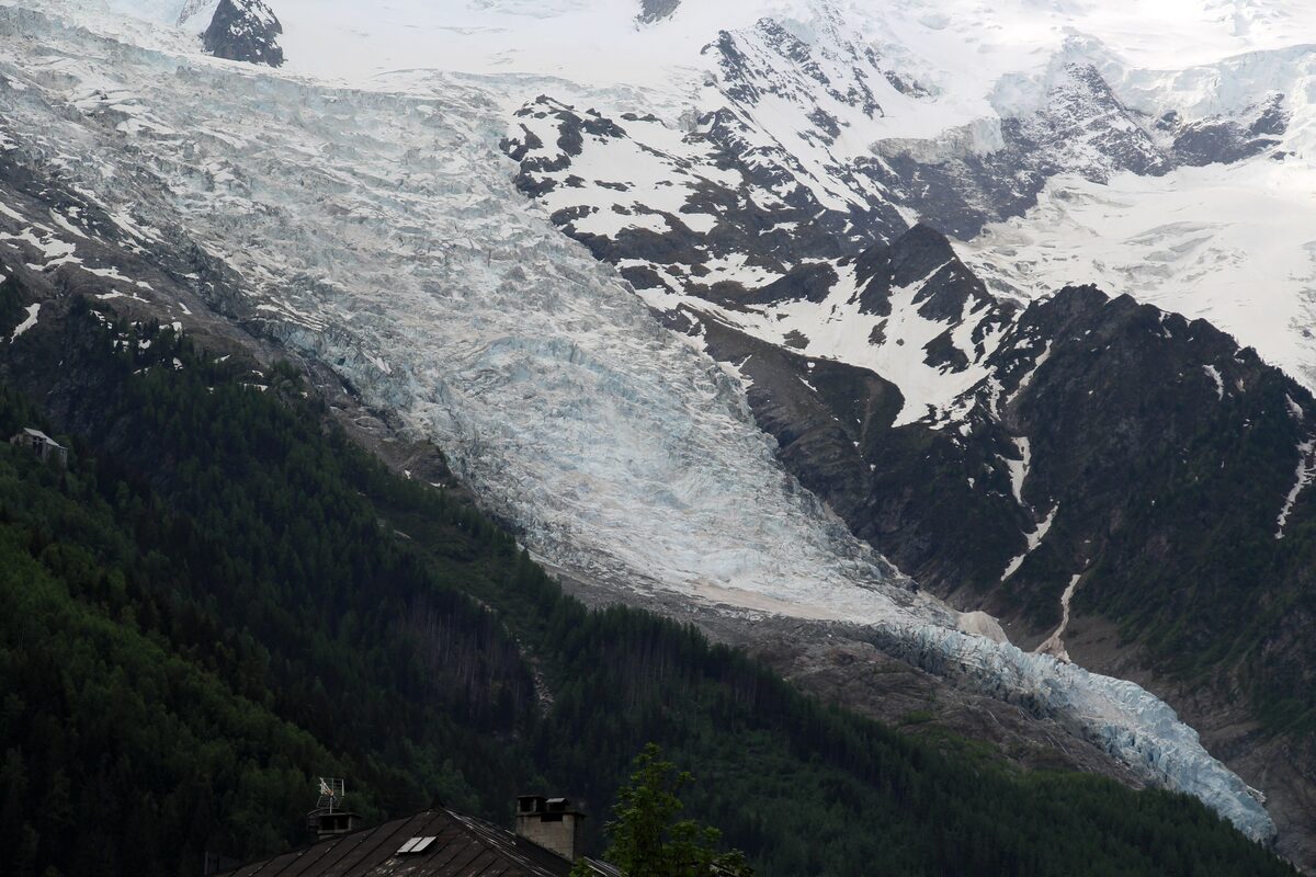 A long glacier tongue flowing down between snow-covered rock peaks and dark forested slopes above the valley